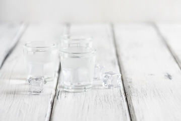 Cold vodka in shot glasses with ice cubes on a white wooden background. Side view, selective focus, copy space. - 754285901