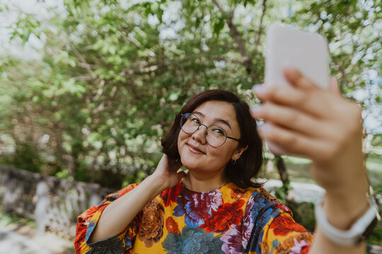Smiling freelancer wearing a colorful blouse taking a selfie outdoors with her smartphone. Business casual professional taking a selfie on her cell phone while enjoying nature
