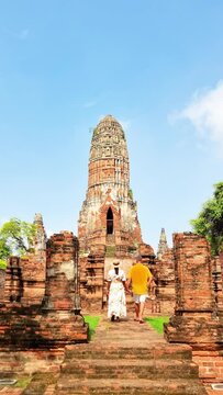 A man and a woman descend the stairs of a historic temple, surrounded by ancient trees, showcasing the art and history of the holy site during their travel adventure Ayutthaya, Thailand