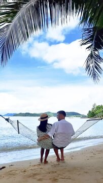 A couple enjoying a peaceful moment in a hammock on the beach, surrounded by the sound of crashing waves and a beautiful sky above. Perfect setting for a relaxing vacation Koh Mak, Thailand