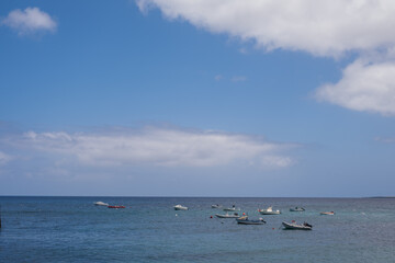 Fototapeta na wymiar Seascape. Group of boats anchored near the pier. Turquoise Atlantic Ocean. Big white clouds. Village of Arrieta. Lanzarote, Canary Islands, Spain