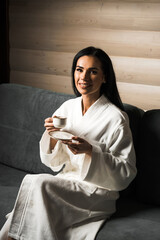 Young woman in a white bathrobe drinks espresso coffee in a wooden hotel room. Hotel holiday concept. Morning coffee