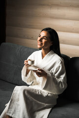 Young woman in a white bathrobe drinks espresso coffee in a wooden hotel room. Hotel holiday concept. Morning coffee