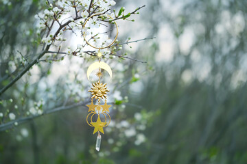 wiccan golden amulet with sun, moon, stars and crystal on blossoming cherry tree, natural abstract...