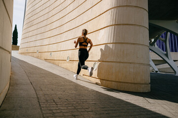 Back view of woman athlete in sportswear is running on buildings background. Active lifestyle...