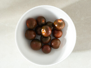 Flat lay view of rare Black Krim heirloom tomatoes in white bowl against pale tiled background
