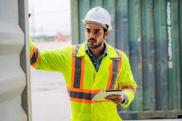 A man in a yellow safety vest is holding a tablet while standing next to a container. Concept of work and productivity, as the man is likely using the tablet for work-related tasks