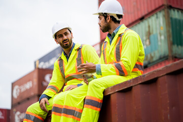 Two men in safety gear are sitting on a rail. One of them is holding a drink. Scene is casual and relaxed