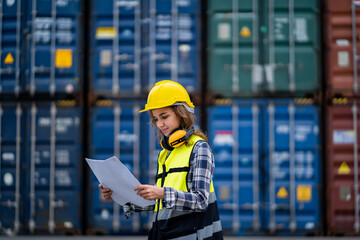 A woman wearing a yellow vest and hard hat is reading a clipboard. She smiles and she enjoys her...