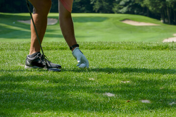 man teeing golf ball on a NH golf course with fairway, sand traps, and green visible