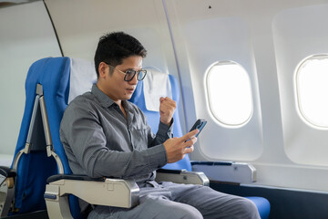 Young professional Asian man working with laptop computer and smartphone while sitting in airplane...