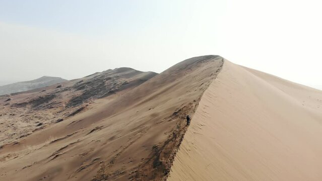 A tourist climbs the crest of a huge sand dune. Desert terrain. Aerial view taken from a drone. Singing dune. Altyn-Emel National Park
