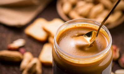 Peanut butter. Creamy smooth peanut butter in jar on a table. Spoon of natural organic vegan food. American cuisine