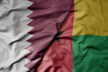 big waving national colorful flag of guinea bissau and national flag of qatar.