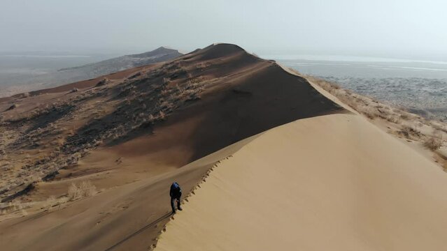 A male tourist walks along the top of a large, long, sand dune. Empty terrain. An aerial view taken from a drone. Singing barchan. Altyn-Emel National Park