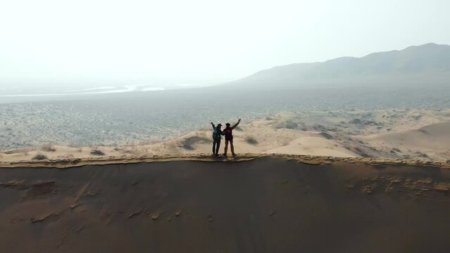 Two hikers on top of a large, sand dune. Rejoicing in their achievement. An aerial view taken from a drone. Singing barchan. Altyn-Emel National Park