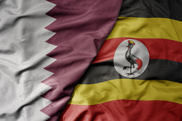 big waving national colorful flag of uganda and national flag of qatar.