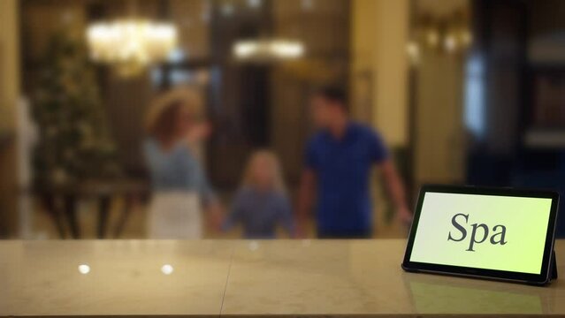 A family on holiday approaches to the reception desk with a tablet labeled spa