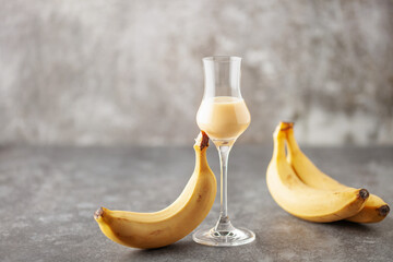 Banana liqueur in grappas glasses and fresh  bananas on the table. Copy space