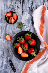 top view, on the textured background, a bowl and a black plate with delicious red strawberries.