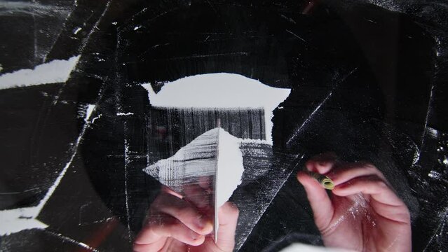 Hand separates cocaine powder with a plastic bank card on a transparent surface in preparation for use