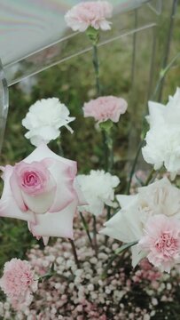 VERTICAL VIDEO. Close-up floristic composition for wedding ceremony arranged with tender pink and white flowers is in a park with trees on greem lawn, slow motion.