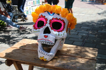 Calavera pintada y con una corona de flores, sobre una mesa de madera en una plaza en Oaxaca,...