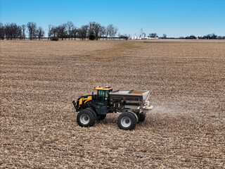 Self propelled spreader applying fertilizer to a field before tilling with farm scene in the...