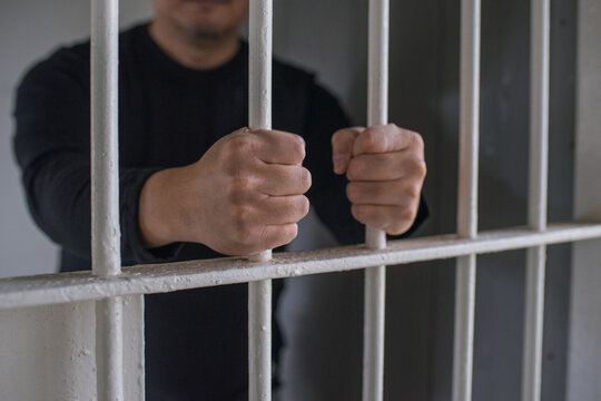檻に閉じ込められた男性　鉄格子を掴む刑務所の犯罪者　Hands of prisoner holding bars in jail