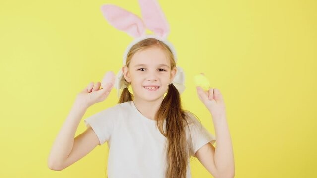 Cute little girl kid wears pink hare ears, holds colored easter eggs grow isolated over yellow background. Look at this decorated Easter eggs!