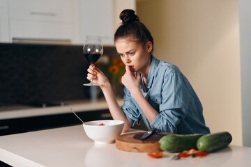 Solitary Reflection: A Sad, Beautiful Woman Sitting Alone at Home, Holding a Glass of Wine on a White Kitchen Table.