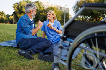 Wheelchair-bound man and nurse enjoying a burger picnic in the sun