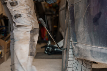 A mechanic repairs a car chassis. A man removes car wheels using a pneumatic screwdriver