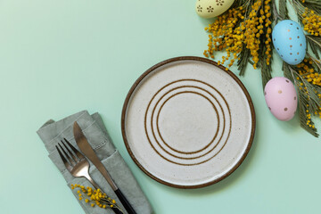 Table setting for Easter dinner with easter eggs and mimosa on a pastel background.