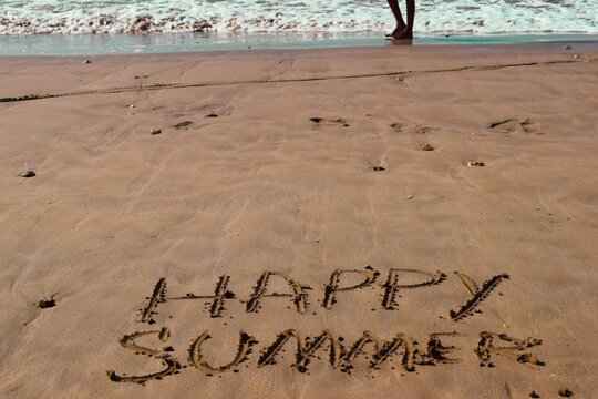 happy summer concept written on sandy beach
