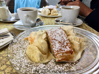 Café table with coffee cups and a glass plate with delicious Apfelstrudel with icecream and whipped cream outdoors in Germany in summer.