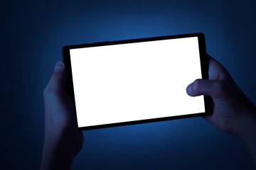 A teenager holds a tablet with two hands at night. Phone with white screen on defocused dark blue...