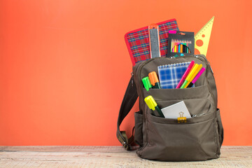 Backpack with different colorful stationery on table. Orange background. Back to school.