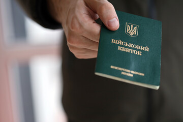 Young ukrainian conscript soldier shows his military token or army ID ticket indoors close up