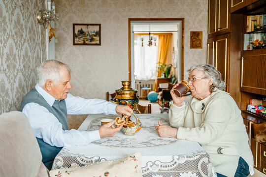Elderly senior romantic love couple drinking tea with cookies from samovar. Old retired man woman together. Aged husband wife in cozy home. Elder people. Happy family longevity. Tender relationships