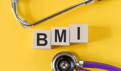 The word BMI is written on wooden cubes near a stethoscope on a yellow background. BMI - body mass index. Medical concept.