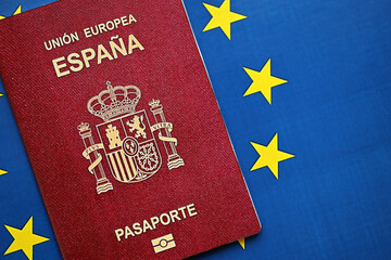 Red Spanish passport of European Union on blue flag background close up. Tourism and citizenship concept - obrazy, fototapety, plakaty