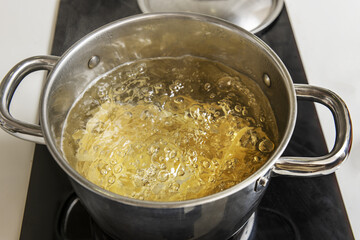 Wheat noodles cooked inside a stainless steel pot filled with boiling water on a black ceramic hob