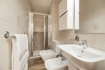 Bathroom with white porcelain toilets, single sink, beveled glass mirror, square stoneware floors and shower cabin with folding screens