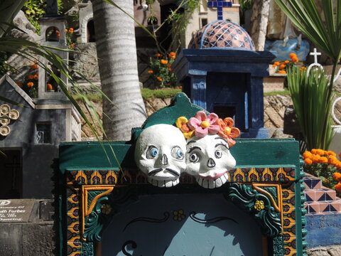 Mystical Tribute: Colorful Tomb Detail with Skull Sculptures, Orange Flowers, and Blue Sky in Mexico for the day of the death