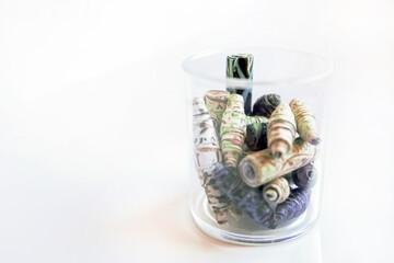 Handmade paper beads of brown, green, black colored floral patterns in plastic glass on white table side view