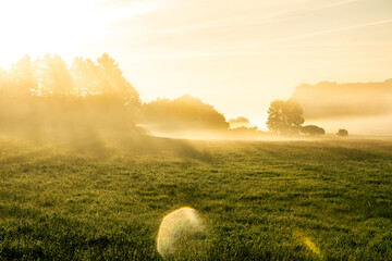 Beautiful sunrise in rural landscape with sun rays shining through the morning fog