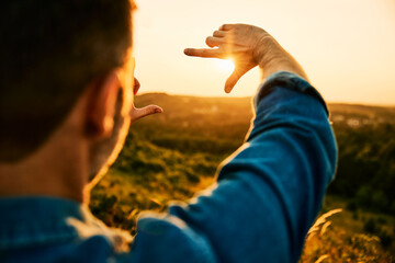 Picture of man shaping frame with his fingers during sunset