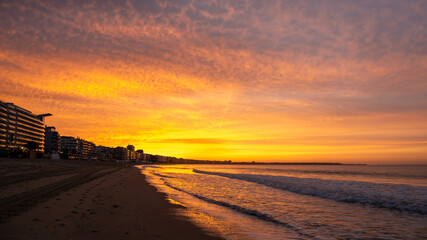Amazing view of a fiery sunrise with multicolored clouds. Sea waves along the seashore at sunrise....