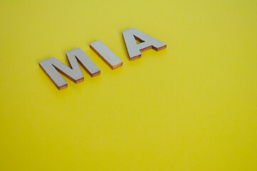 MIA wooden letters representing Missing In Action on yellow background